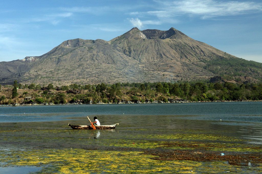 A person riding a boat on Batur Lake with the Mount Batur in the background in Bali, Indonesia.