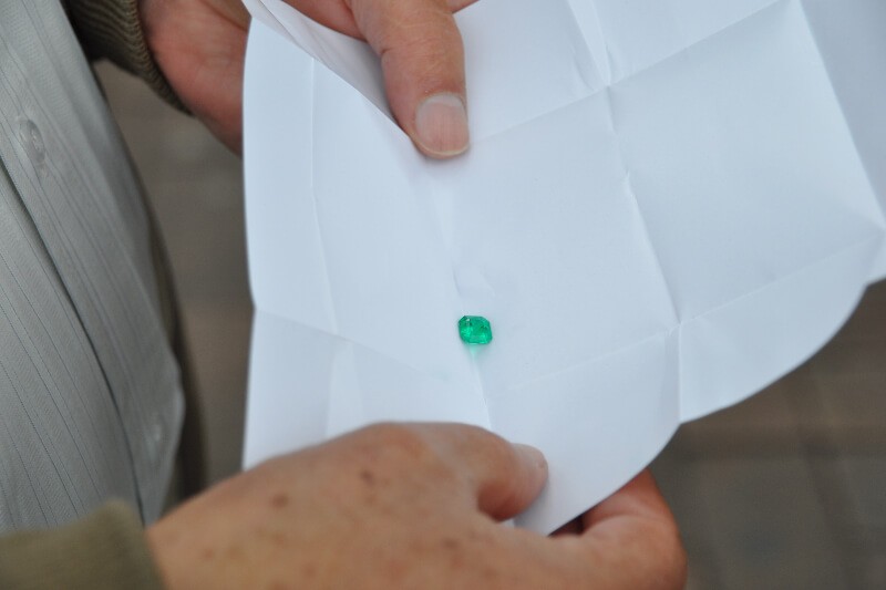 A piece of emerald on white paper being held by two hands.