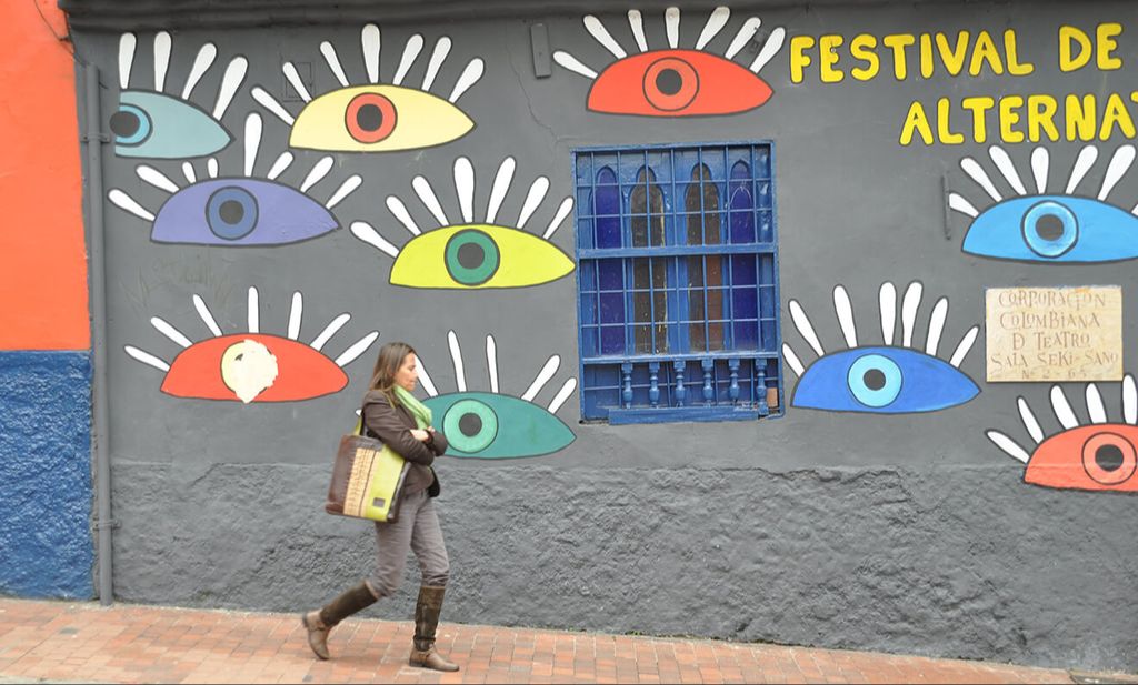 A woman walking on a street with a wall with wall art in the background in Bogota, Colombia.