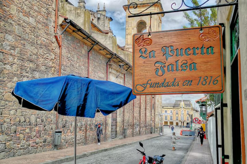 A street with a wooden sign that says, ""La Puerta Falsa fundada en 1816."