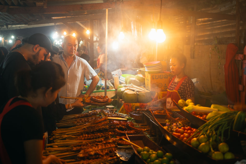 People buying and selling skewers at a market in Laos.