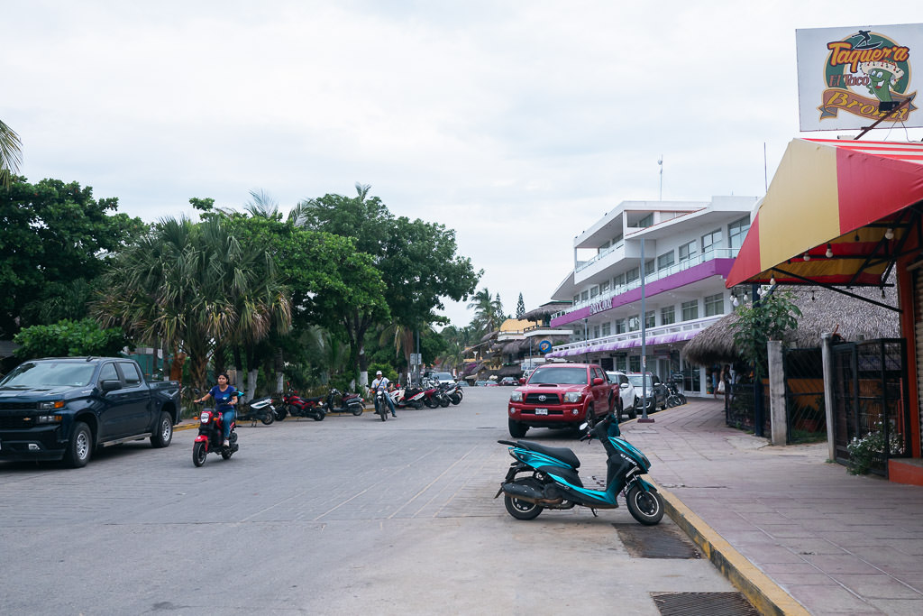 Playa Zicatela town road with parked cars and motorcycles.