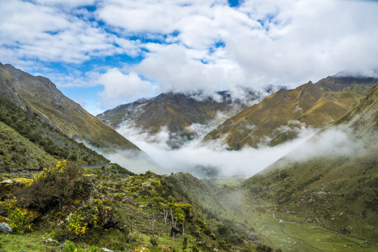 Salkantay Trekking Peru A hazy, high-altitude view of the Salkantay Trail, with mist filling the valleys between steep, grassy mountains.