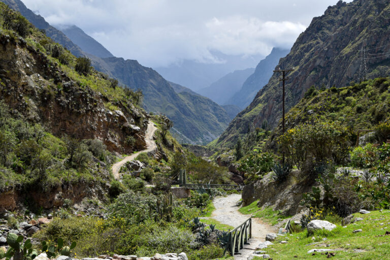 View of the beginning of the classic Inca trail to Machu Picchu A winding dirt path leads through a lush green valley towards distant mountains, flagging the beginning of the Inca Trail to Machu Picchu